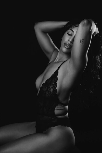 black and white boudoir picture of woman grabbing her hair and looking down in a sexy and elegant pose