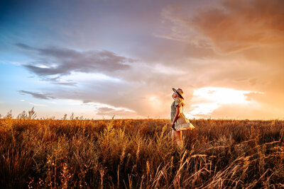 Nebraska Senior photographer | senior stands in field at sunset holding hat