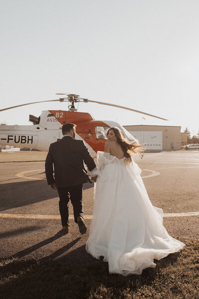 Couple walking towards a helicopter on a tarmac, bride in a flowing white dress.