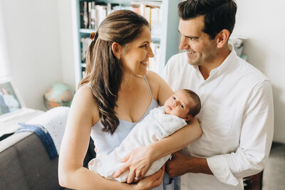 Mom holds baby while dad looks at her lovingly in-home SF