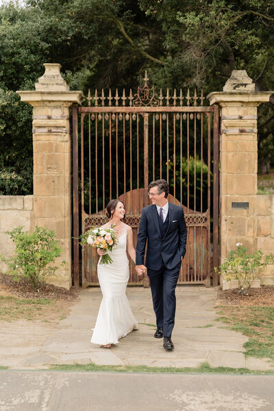 Bride and Groom walking holding hands in front of gate at their wedding at Vista Valley wedding venue