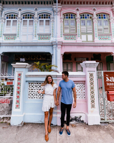 man and woman holding hands in front of blue and pink building