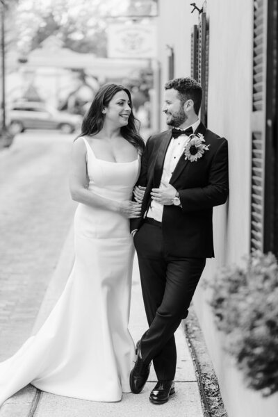 Bride holding grooms arm on a sidewalk against a building