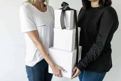 white gift boxes tied with black ribbon being held by two white women