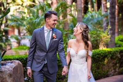 Bride and groom laughing and holding hands amid the nature at Grand Tradition Estate and Gardens wedding venue in San Diego.