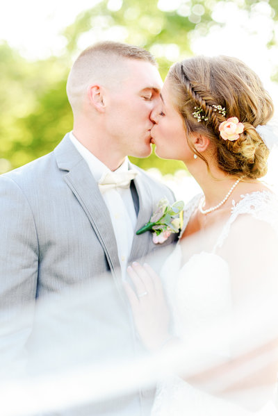 Bride and groom kiss with veil sweeping in front of them.