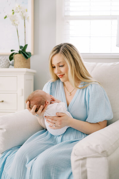 Mom holds newborn baby girl sitting in white nursery chair