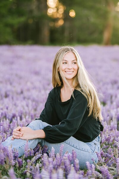 Senior girl sitting smiling on a bed of purple short lupines at Prosser in Truckee close to sunset.