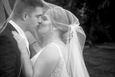Black-and-white-image-of-bride-and-groom-kissing-underneath-her-veil