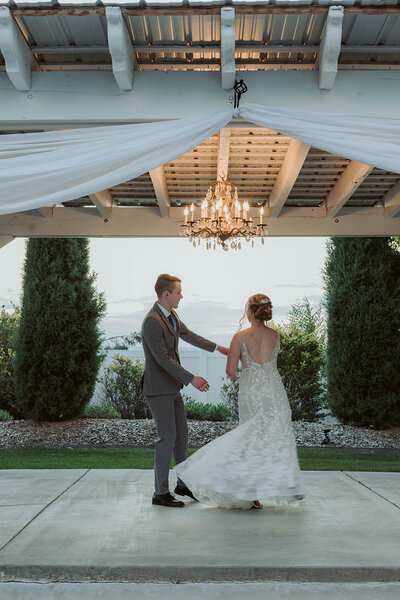 A bride and groom dance under a chandelier in an outdoor pavilion surrounded by trees, capturing real moments during their Colorado wedding day.
