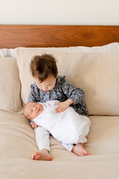 baby wrapped in white swaddle is held by older sibling in Pacific Palisades