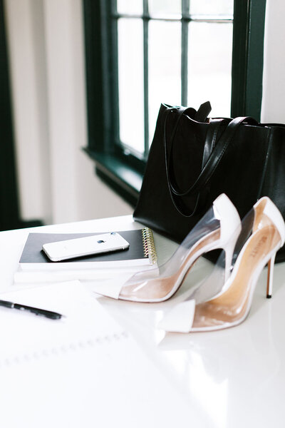 Photo of a kitchen table with a phone, purse, and white heels.