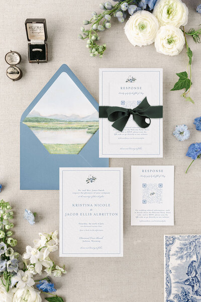 An elegant wedding invitation suite showcases a custom watercolor venue illustration as the envelope liner, paired with an emerald silk ribbon and letterpress printing for a refined and tactile touch.