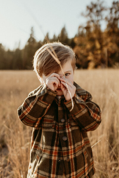 A little boy in a plaid shirt standing in a field.