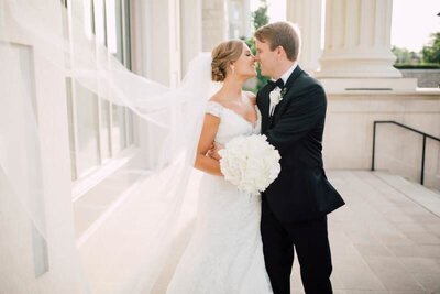 Bride and Groom on steps snuggled nose to nose with veil in air
