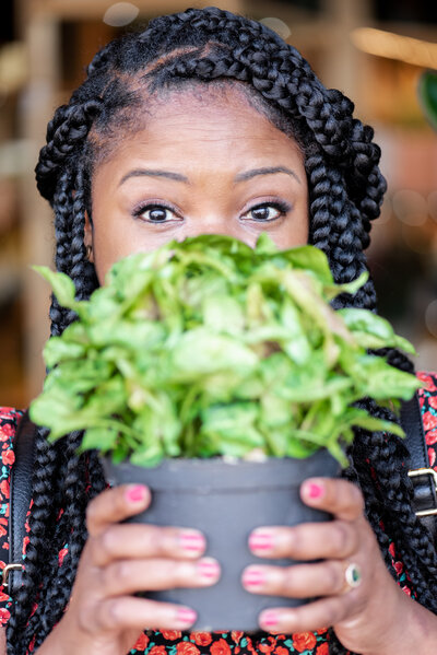Woman holds a plant in front of her face hiding her moth.