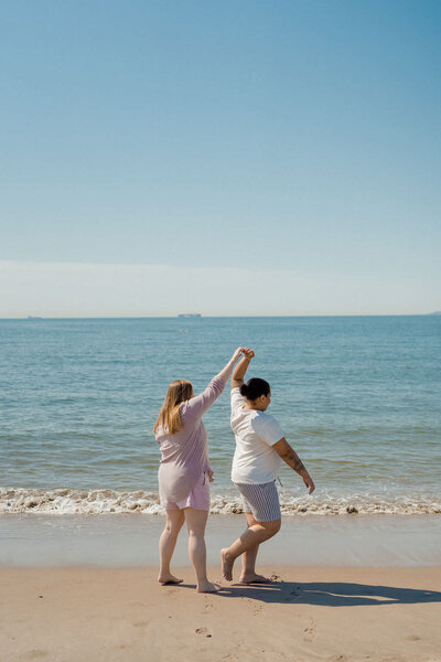 person spinning their partner around as they walk along the shoreline of a beach