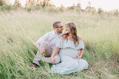 Expectant mother in green dress in portland field of grass looking back at husband smiling