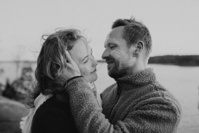 Kihlapari hymyilee ja katsoo toisiaan ja mies pitelee naisen kasvoista toisella kädellään kiinni meren äärellä Kivenlahdessa Espoossa