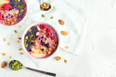 Two colorful smoothie bowls topped with fresh berries and crunchy nuts, served on a wooden table.