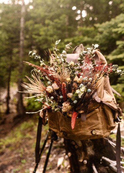 a dried bridal bouquet hangs out of a backpack  during a washington elopement
