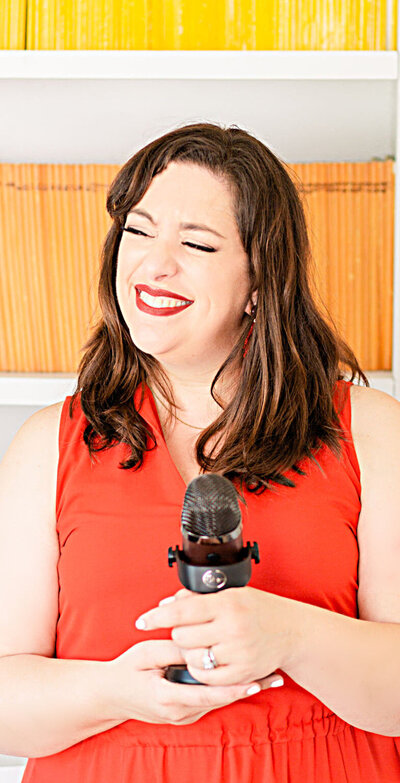 Podcast host, Renee Dalo, smiles in red blouse with podcast mic