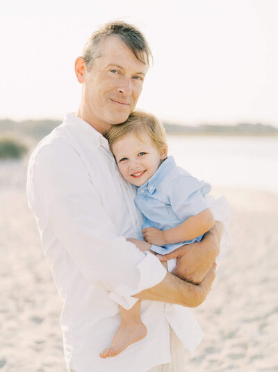 Formal portrait of a father and son dressed in white on the beach.