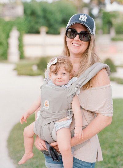 Mom in baseball cap wears baby in sling