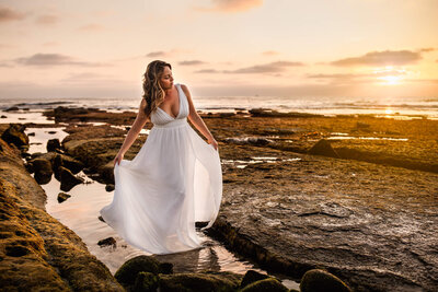Woman in Lulus white dress standing in tide pool at Windansea Beach in San Diego
