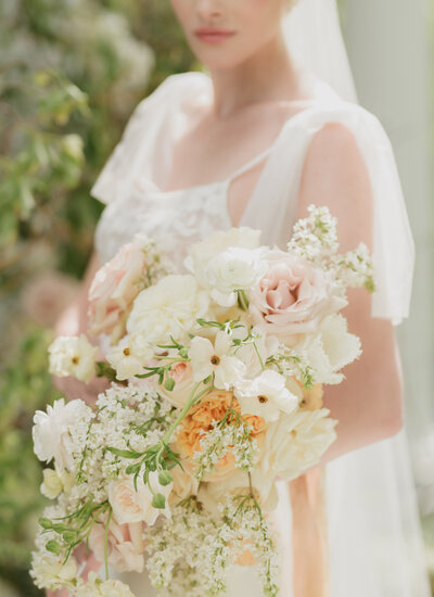 white bride holding stunning summer floral bouquet. with white, pink and orange florals.