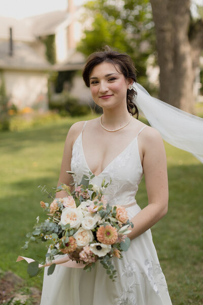 bride is standing with her veil blowing in the wind and holding flowers