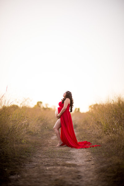 Maternity photo of San Antonio Photographer Irene Castillo standing in a field golden grass at sunset
