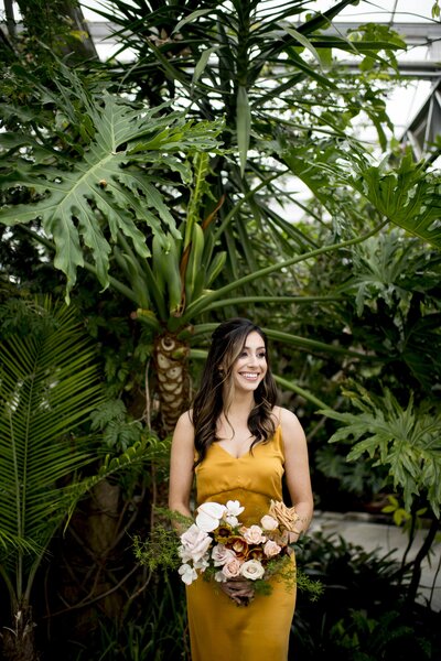 Model in yellow dress holding bouquet standing in front of greenery - Part of Wedding Content Shoot