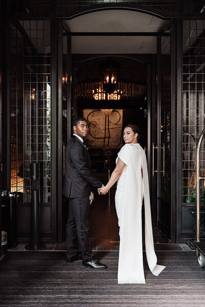 bride and groom stand holding hands in the entrance to the nomad hotel looking back at the camera on their wedding day