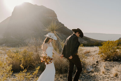 A couple walking through the desert in West Texas, eloping and holding a bouquet of flowers.