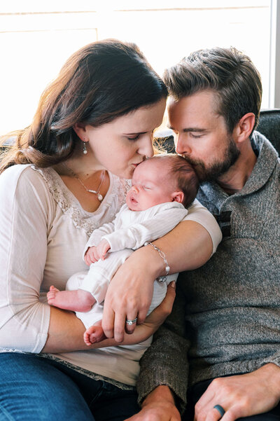 Northern Virginia family photographer photographs a young family holding their infant son and giving him a kiss on top of the head