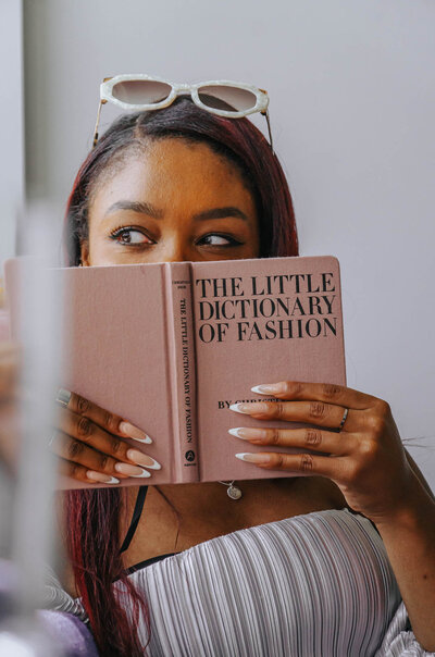 Tahirah playfully holding up a copy of "The Little Dictionary of Fashion" so it covers her face up to her eyes