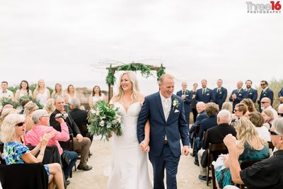 Bride and Groom walk down the aisle amongst wedding guests while holding hands