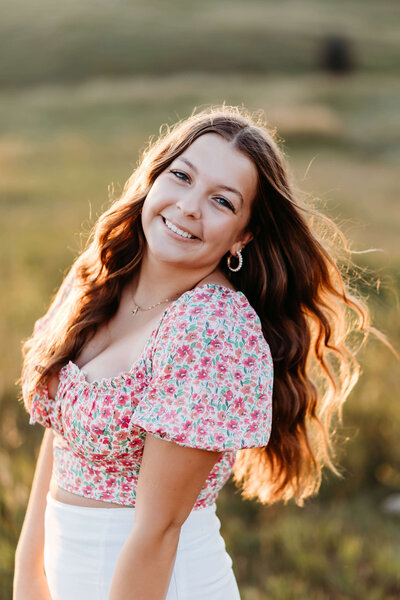 Senior girl leaning on bridge with sun peaking out of the trees behind her.