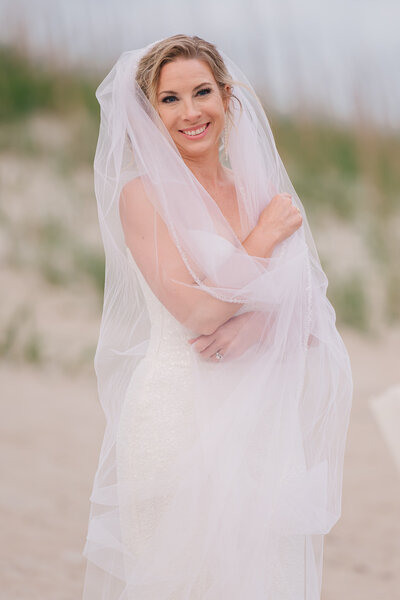 A smiling blonde bride on the Wilmington coastline enjoying her Wilmington wedding photography bridal portrait session by JoLynn Photography