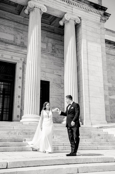 black and white photo of groom leading bride down steps