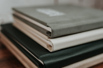 Neat pile of beautiful leather wedding albums in forest green, cream and sage green