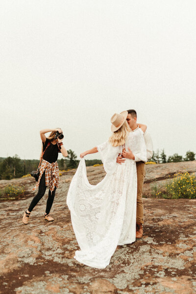 Elopement photographer holding camera and taking picture of boho bride and groom