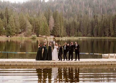 Wedding party standing on boat dock and raising hands in celebration in Sequoia National Forest