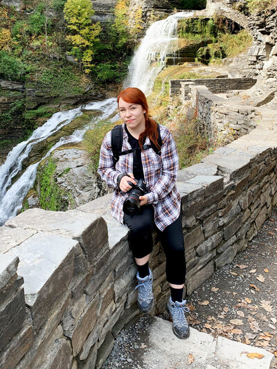 photographer holding camera next to waterfall