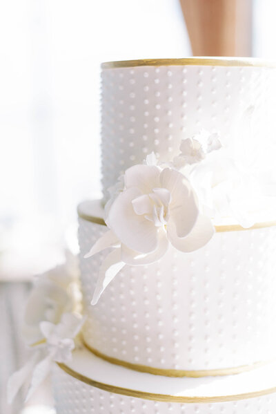 white and gold simple wedding cake with a large white flower on the side