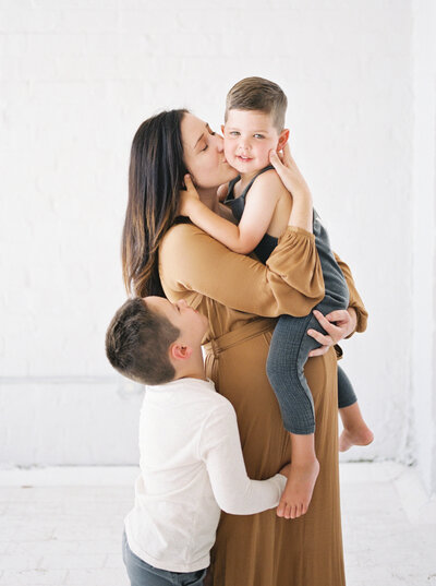 expecting mother in beautiful dress holding children in white studio by Madison WI photographer Talia Laird Photography