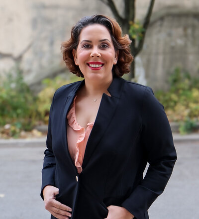 A woman named Ida Salusky wearing a black blazer over a pink shirt, standing confidently.