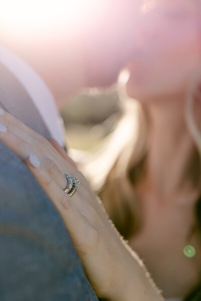 detail of a wedding ring. Behind it a kiss of the newlyweds and sunset light.