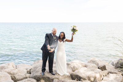 Bride-and-groom-celebrate-by-spraying-champagne-on-the-rocks-after-their-waterfront-intimate-wedding-elopement